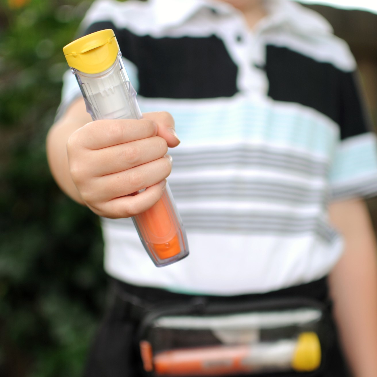 Child holding an epinephrine auto-injector, with another one shown in a small pouch around the child's waist.